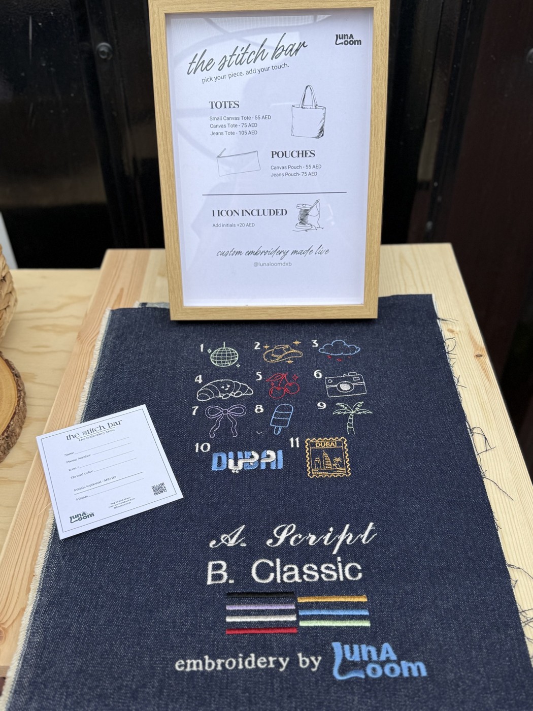Lunaloom embroidery menu and framed sign displayed at an event